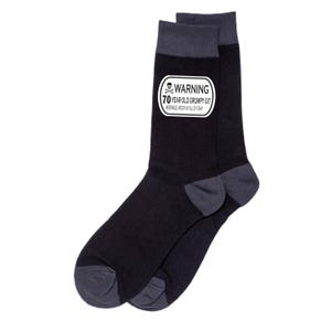 May include: A pair of black socks with gray accents at the toe and cuff. A white rectangular patch on the side of the sock reads "WARNING 70 YEAR OLD GRUMPY GIT MISERABLE, MOODY & FULL OF CRAP" in black text.