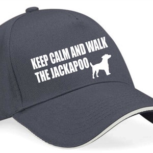 Może przedstawiać: Czapka bejsbolowa w kolorze granatowym z białym daszkiem i napisem "Keep Calm and Walk the Jackapoo" w białym kolorze. Na czapce znajduje się również biała sylwetka psa.