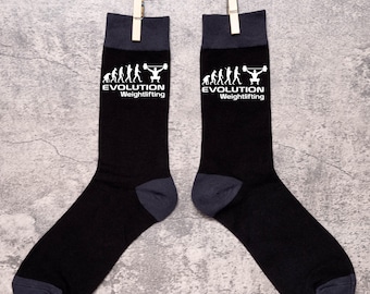 May include: A pair of black socks with a white graphic of the evolution of man culminating in a man lifting weights. The socks have the text "EVOLUTION Weightlifting" on each sock.