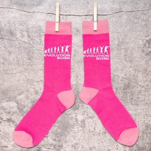 May include: A pair of pink socks with a white graphic of the evolution of boxing. The socks have the text "Evolution Boxing" on them.