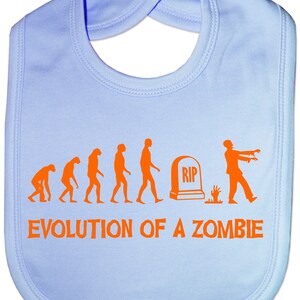 May include: A light blue baby bib with an orange graphic of the evolution of a zombie. The graphic shows a series of stick figures evolving from a primitive ape to a zombie. The text "EVOLUTION OF A ZOMBIE" is printed below the graphic.