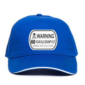 May include: A royal blue baseball cap with a white trim and a white and black patch. The patch reads "WARNING 60 YEAR OLD GRUMPY GIT" with a skull and crossbones symbol.