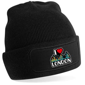 May include: Black knit beanie featuring a rectangular patch with the text "I Love London" and a graphic of the London skyline, including the London Eye and Big Ben. The heart in the graphic is red.