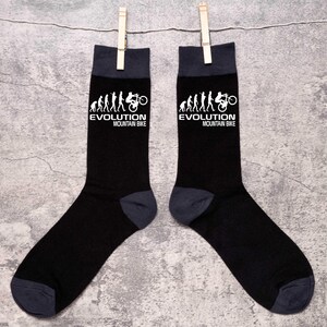 May include: A pair of black socks with dark gray heels, toes, and cuffs. The socks feature a white graphic of the evolution of man to a mountain bike, with the text "EVOLUTION MOUNTAIN BIKE" in white.