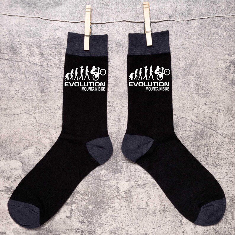 May include: A pair of black socks with dark gray heels, toes, and cuffs. The socks feature a white graphic of the evolution of man to a mountain bike, with the text "EVOLUTION MOUNTAIN BIKE" in white.