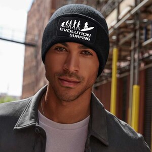 May include: Black beanie with a white patch featuring a silhouette of a person surfing and the text "EVOLUTION SURFING" with a graphic of the evolution of man leading up to the surfer.