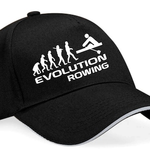 May include: Black baseball cap with a white design of a stick figure rowing a boat and the text "EVOLUTION ROWING" with a series of stick figures representing the evolution of man.