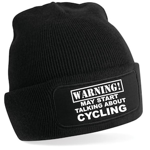 Könnte beinhalten: Schwarze Mütze mit einem weißen Aufnäher, auf dem "WARNUNG! KÖNNTE ÜBER RADFAHREN REDEN" steht.
