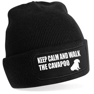 Puede incluir: Gorro de punto negro con un parche blanco que dice "Keep Calm and Walk the Cavapoo" con una silueta blanca de un perro Cavapoo.
