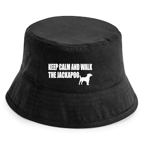 Puede incluir: Sombrero de pescador negro con el texto blanco "KEEP CALM AND WALK THE JACKAPOO" y una silueta blanca de perro. El sombrero, de tejido resistente, tiene un estilo clásico e informal, perfecto para el día a día.