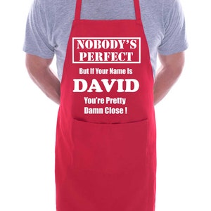 Puede incluir: Delantal rojo con un bolsillo blanco y el texto "Nobody's Perfect But If Your Name Is DAVID You're Pretty Damn Close!"