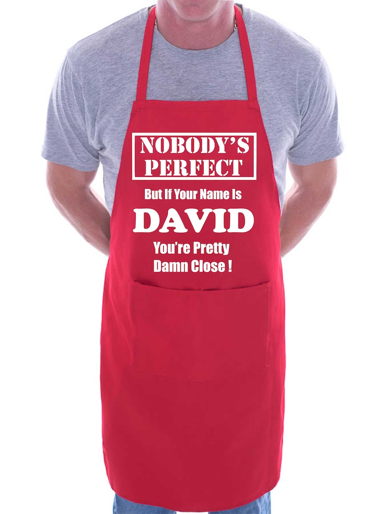 Puede incluir: Delantal rojo con un bolsillo blanco y el texto "Nobody's Perfect But If Your Name Is DAVID You're Pretty Damn Close!"