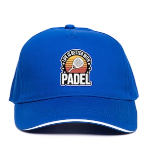 May include: A royal blue baseball cap with a white trim and a circular graphic. The graphic features a padel racket and the text "LIFE IS BETTER WITH PADEL" in a retro sunset design. The cap has a curved peak.