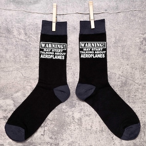 May include: A pair of black socks with a white warning sign that says "WARNING! MAY START TALKING ABOUT AEROPLANES".