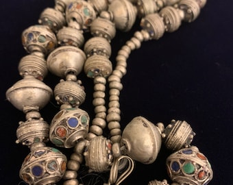 May include: A silver necklace with large, round beads. The beads are decorated with colorful enamel and have a textured surface. The necklace is approximately 30 inches long.