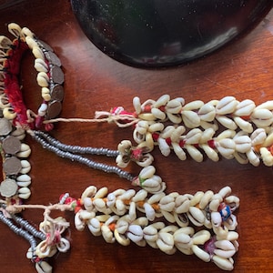 May include: Three strands of white shell necklaces with red, blue, and white accents. The necklaces are made of small, white shells strung together on a thin cord. The shells are arranged in a staggered pattern, creating a visually appealing design.