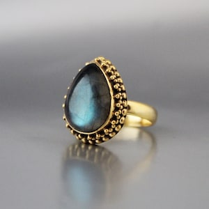Könnte beinhalten: Ein goldener Ring mit einem tropfenförmigen blauen Labradorit-Edelstein, der in einer perlenbesetzten Fassung sitzt.
