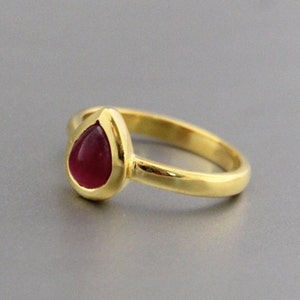 May include: A gold ring with a teardrop-shaped red gemstone.