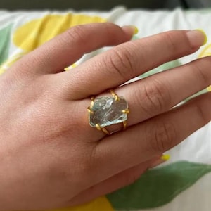 Könnte beinhalten: Ein goldener Ring mit einem großen, klaren, facettierten Aquamarin, der in einem Drahtrahmen gefasst ist.