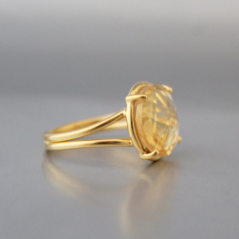 K&ouml;nnte beinhalten: Ein goldener Ring mit einem gro&szlig;en, ovalen, gelben Edelstein, der in einer Krappenfassung sitzt. Der Ringarm ist d&uuml;nn und hat eine geteilte Schiene.