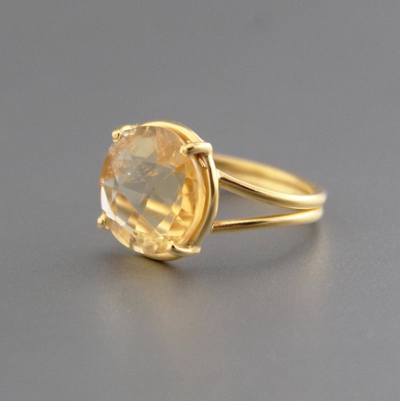 K&ouml;nnte beinhalten: Ein goldener Ring mit einem gro&szlig;en, ovalen, hellgelben Edelstein, der in einer Zargenfassung gefasst ist. Das Ringband ist d&uuml;nn und hat ein Doppelband-Design.