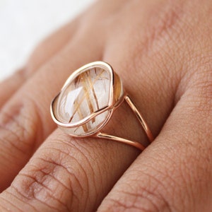 May include: A gold ring with a clear quartz stone featuring golden inclusions. The ring has a delicate, open design.