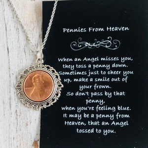 May include: A silver chain necklace with a copper penny pendant. The penny is surrounded by a silver filigree design. The necklace comes with a black card with the text "Pennies From Heaven" and a poem about finding pennies.