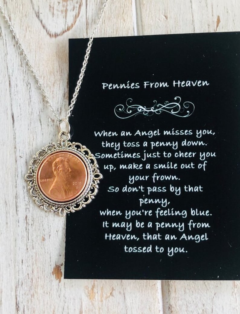 May include: A silver chain necklace with a copper penny pendant. The penny is surrounded by a silver filigree design. The necklace comes with a black card with the text "Pennies From Heaven" and a poem about finding pennies.