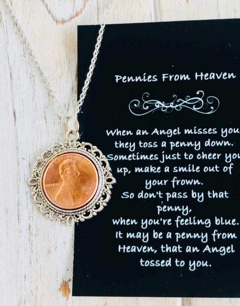 May include: A silver necklace with a copper penny pendant. The pendant is surrounded by a decorative silver frame. The necklace comes with a card that reads "Pennies From Heaven" and a poem about finding a penny.