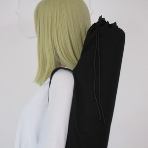 May include: A black yoga mat bag with a drawstring closure is slung over a shoulder. The bag is made of a solid black fabric and has a long, cylindrical shape. The strap is also black. The background is white.