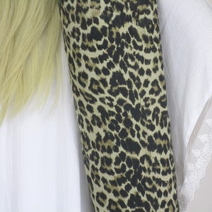 May include: A rolled fabric with a leopard print in shades of black and tan is next to a white garment with lace trim. Blonde hair is visible on the left side of the image. The fabric is the focal point.
