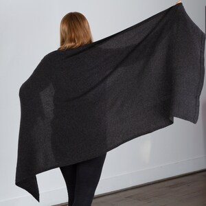 May include: A charcoal gray cashmere wrap, draped over a person's shoulders. The wrap is soft and luxurious, and it would be perfect for keeping warm on a chilly day.