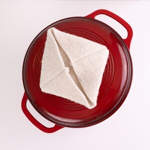 May include: A red cast iron pot with a white fabric lid. The lid is folded into a triangle shape.