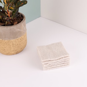 May include: A stack of six off-white cotton rounds, arranged in a square shape, on a white surface.
