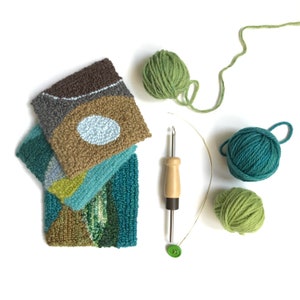 May include: A set of four colourful rug hooking kits with a wooden needle, green yarn, and a green button. The kits feature geometric shapes in shades of brown, green, blue, and white.