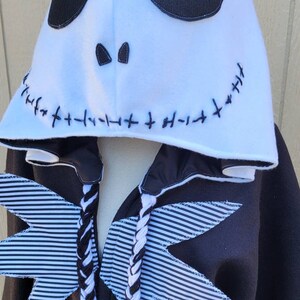 May include: Black and white striped fabric wings with a white hooded sweatshirt featuring a black stitched Jack Skellington face. The hood has a white fleece lining.