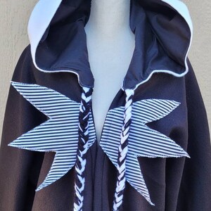 May include: Black hooded robe with white striped star accents and white and black braided ties.