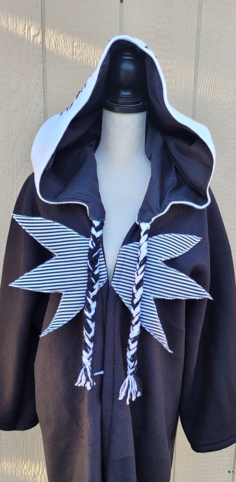 May include: Black hooded robe with white striped star accents and white and black braided ties.