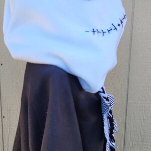 May include: Black and white hooded sweatshirt with a white fleece hood featuring a black stitched Jack Skellington face. The hood has a black and white striped tassel.