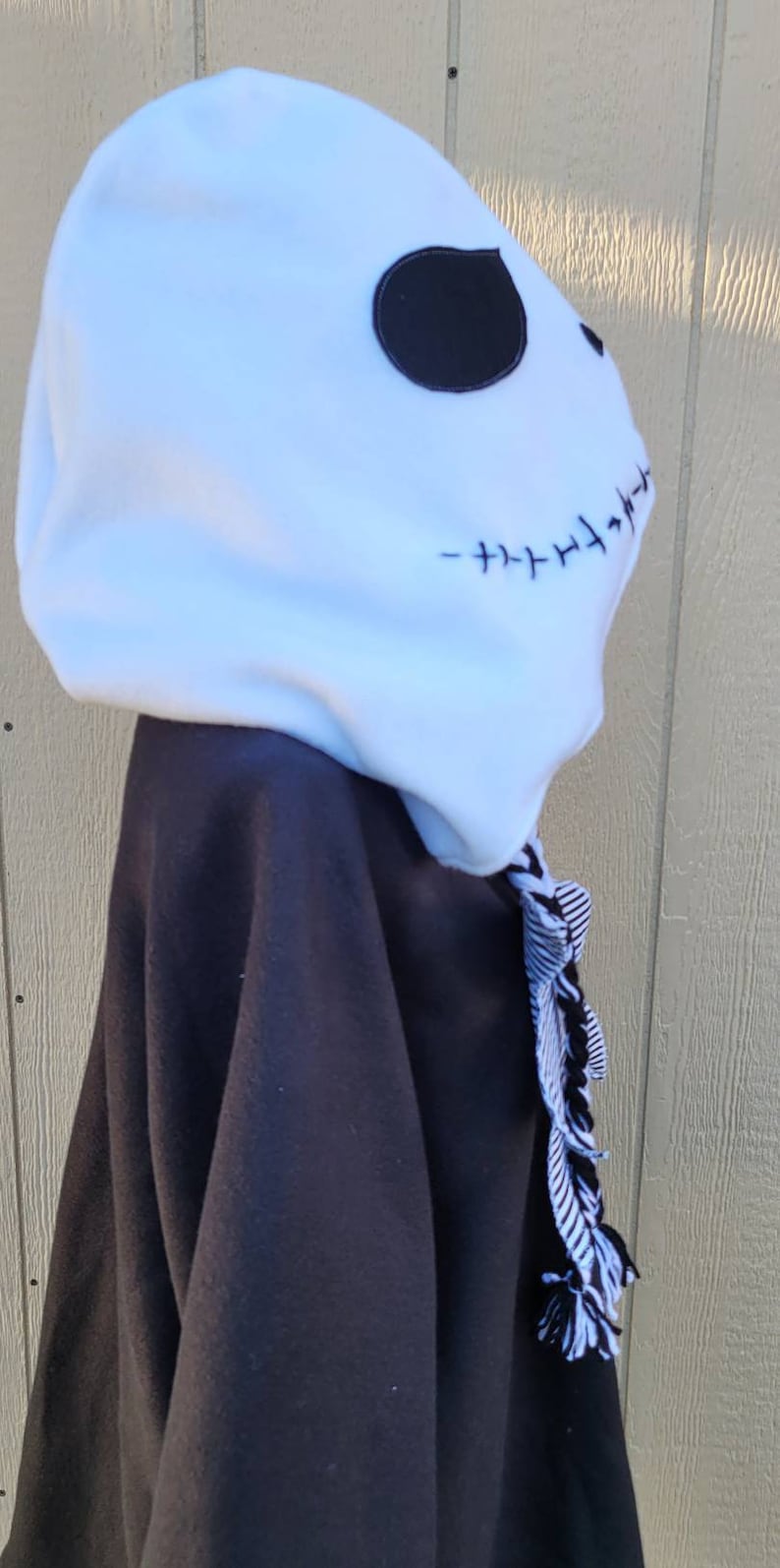 May include: Black and white hooded sweatshirt with a white fleece hood featuring a black stitched Jack Skellington face. The hood has a black and white striped tassel.