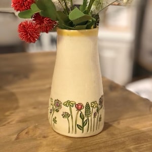 May include: A white ceramic vase with a yellow rim and a floral design. The vase is filled with red and white flowers.