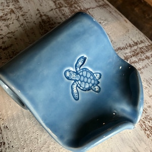 May include: A light blue ceramic soap dish with a raised design of a sea turtle.