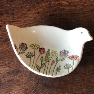 May include: White ceramic bird-shaped dish with a floral design. The flowers are painted in shades of pink, purple, yellow, and green.