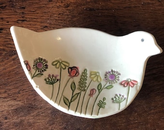 May include: White ceramic bird-shaped dish with a floral design. The flowers are painted in shades of pink, purple, yellow, and green.