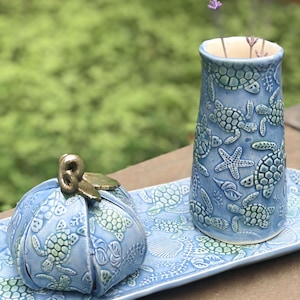 May include: A blue ceramic tray with a blue ceramic vase and a blue ceramic pumpkin with a gold top. The tray, vase, and pumpkin are decorated with sea turtles and other sea life.