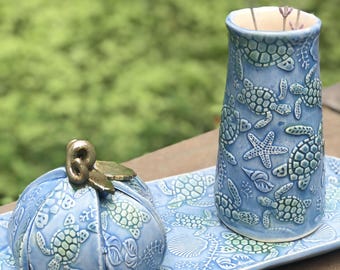 May include: A blue ceramic tray with a blue ceramic vase and a blue ceramic pumpkin with a gold top. The tray, vase, and pumpkin are decorated with sea turtles and other sea life.