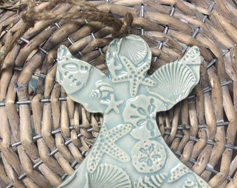 May include: A light blue ceramic angel ornament with a seashell design. The ornament is decorated with seashells, starfish, and sand dollars.