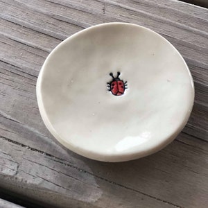 May include: A small white ceramic dish with a red ladybug design.