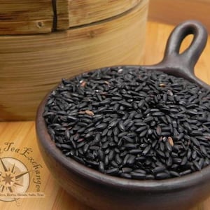 May include: A close-up of a bowl of black rice. The rice is in a brown ceramic bowl with a handle. The bowl is sitting on a wooden surface.