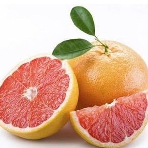 May include: A close-up of a grapefruit, with one whole fruit, a half, and a wedge. The grapefruit has a yellow rind and red flesh. Green leaves are attached to the whole fruit. The background is white.